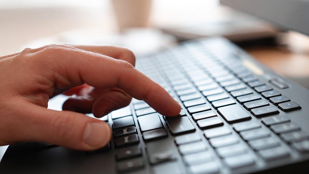A photograph of a hand pressing the "Send" key on a keyboard in a blurred indoor setting.