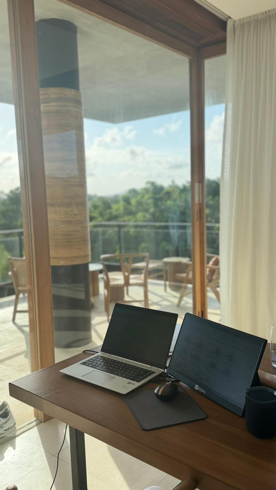 Laptop and iPad sitting on a desk with a view of Uluatu, Bali in the background.