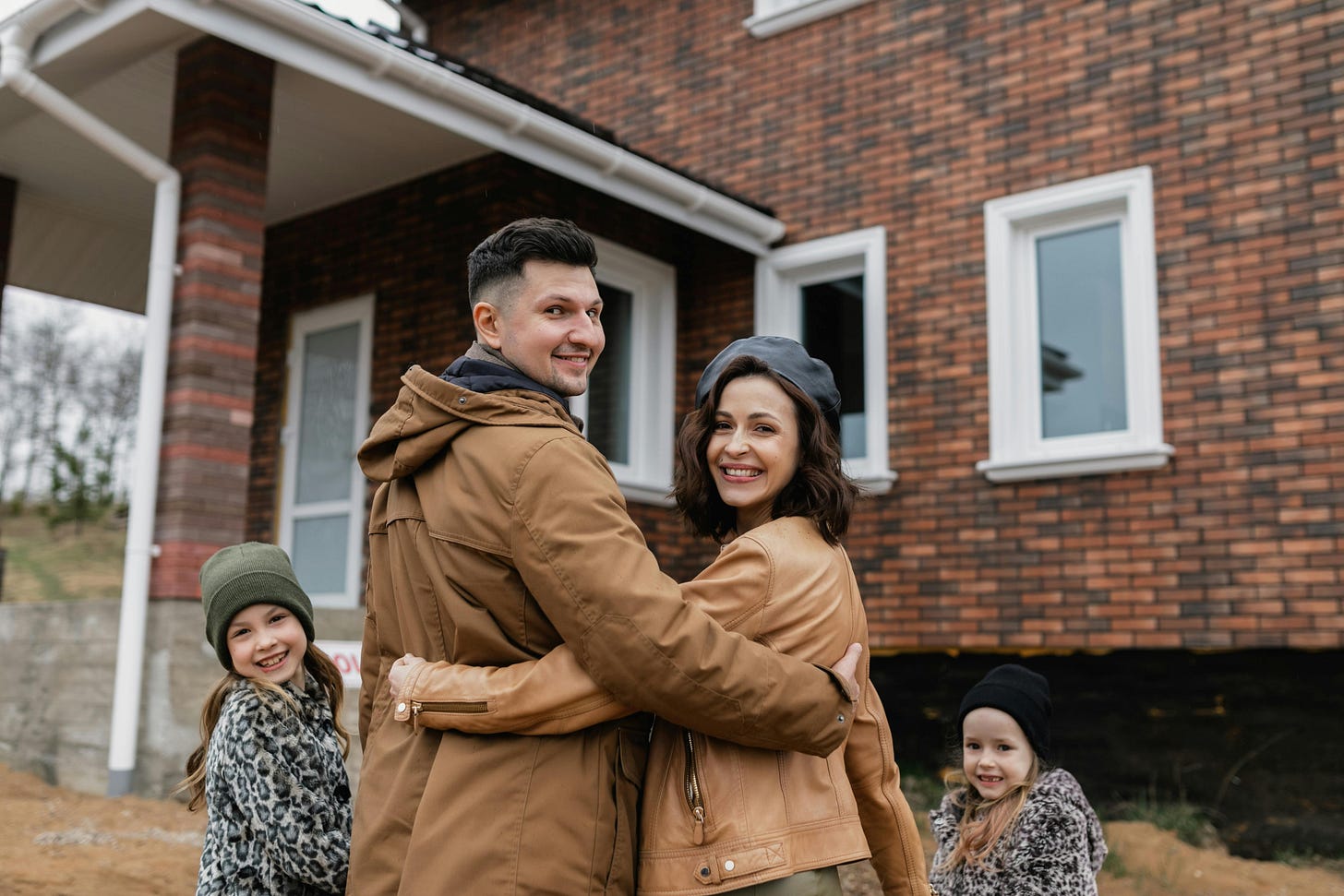 Family with two kids in front of a house, everyone is smiling. Family with two kids in front of a house, everyone is smiling.
