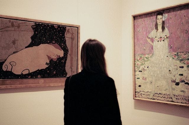 This may contain: a woman standing in front of two paintings on the wall and looking at one another