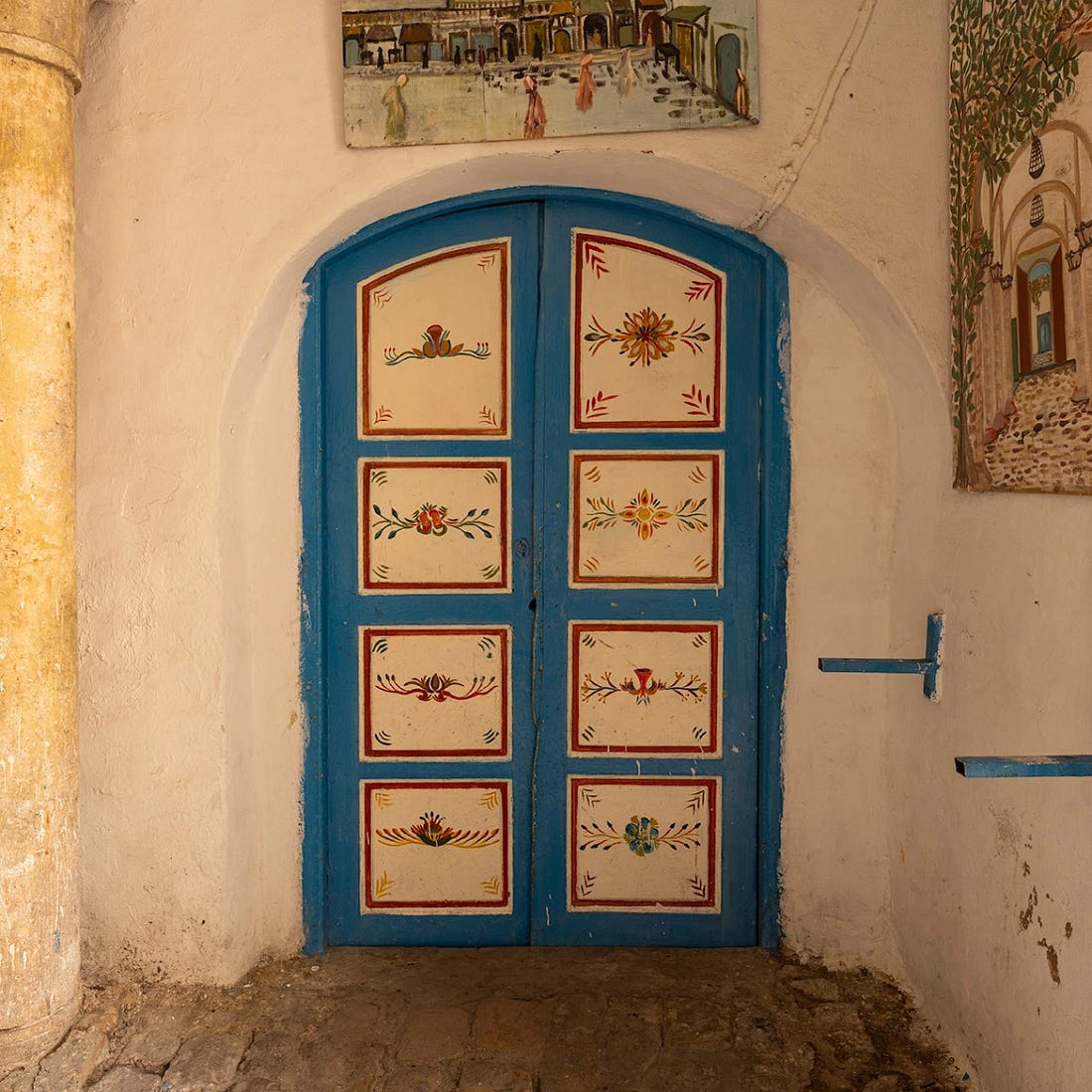 Hand-painted blue double doors set into a whitewashed wall in the Tunis Medina, decorated with floral motifs and framed by worn stone and tiled details.