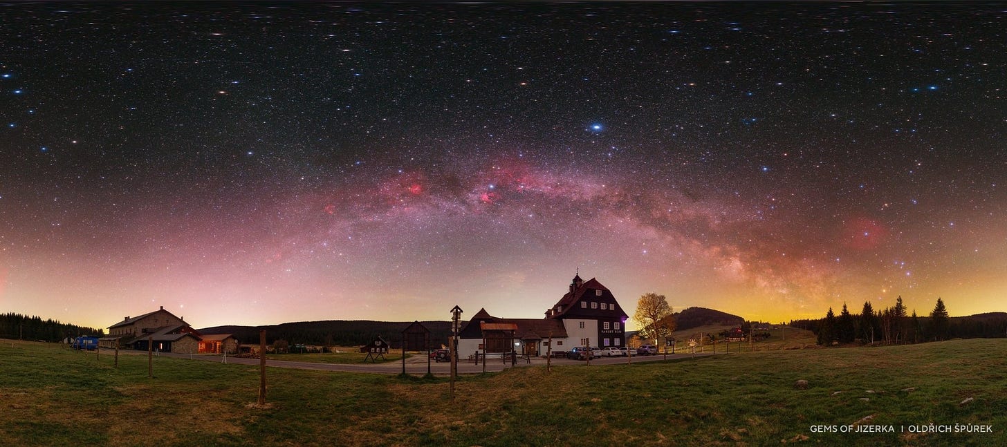 A wide field view of rural houses under a clear night sky features the Milky Way arching brightly overhead, reminiscent of 2025 night sky images with countless stars visible above the horizon.