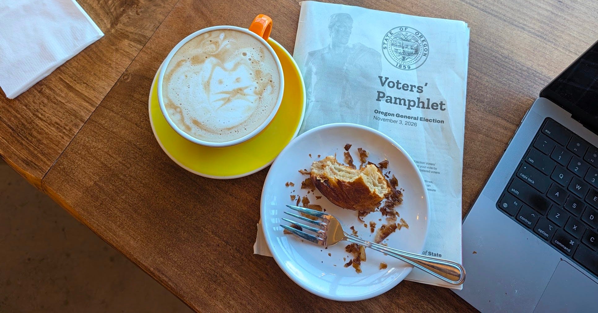 Close-up view of a latte, half-eaten croissant, and the Oregon Voter's Guide for November 3, 2026 Close-up view of a latte, half-eaten croissant, and the Oregon Voter's Guide for November 3, 2026
