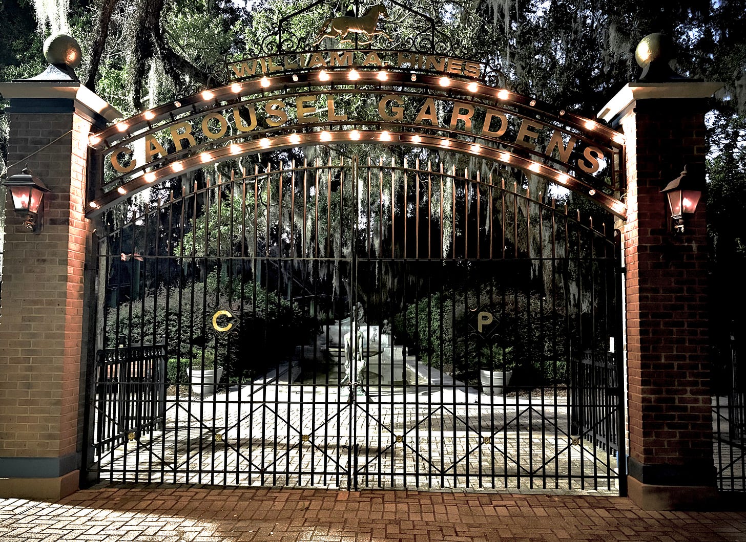 photo of big iron gates, tall trees covered in Spanish moss, and shadows