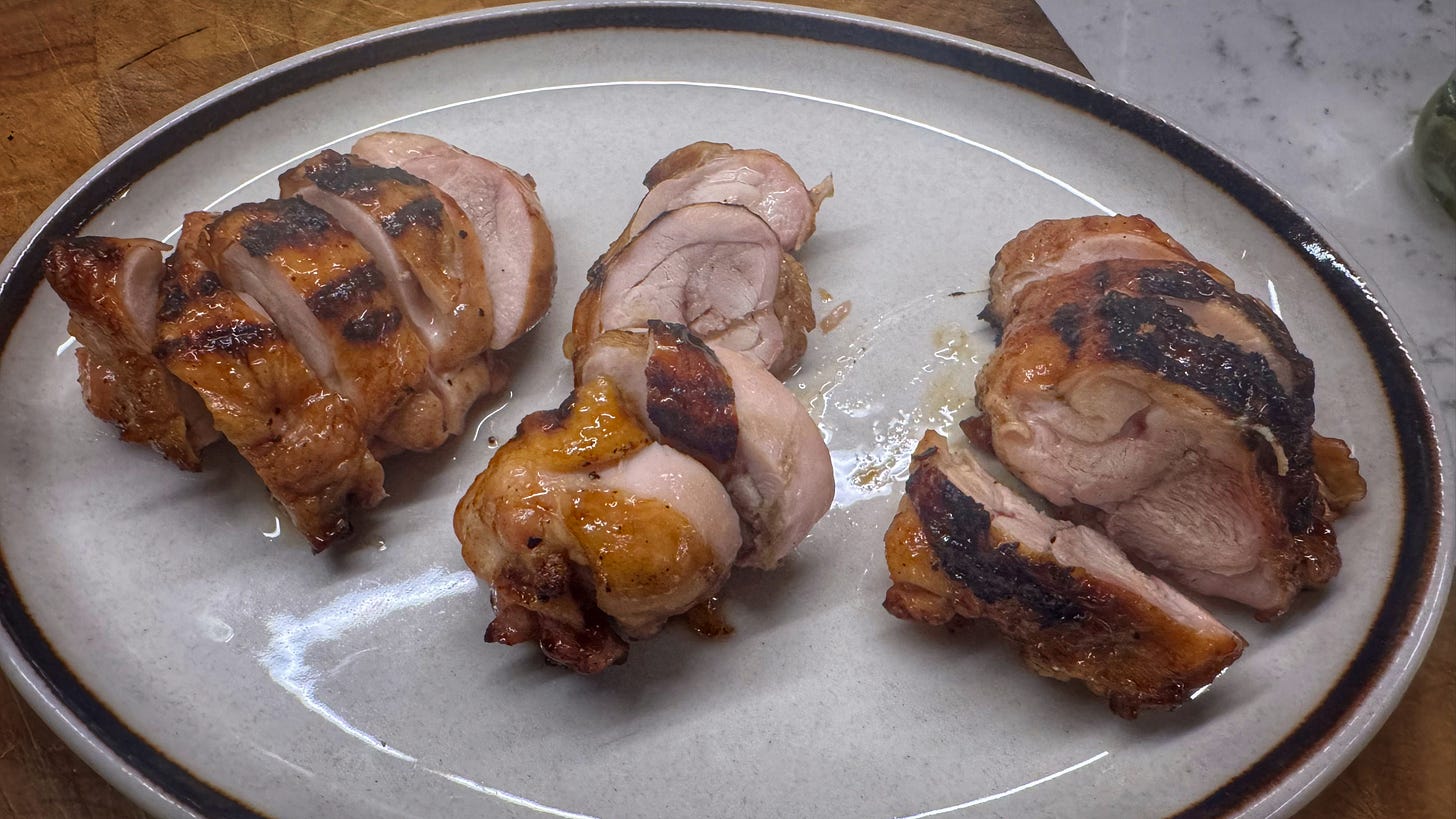 A serving plate holding three of the grilled chicken thighs. They have now been sliced into four pieces each and we can see the cooked meat inside. The plating is not particularly attractive or artful.
