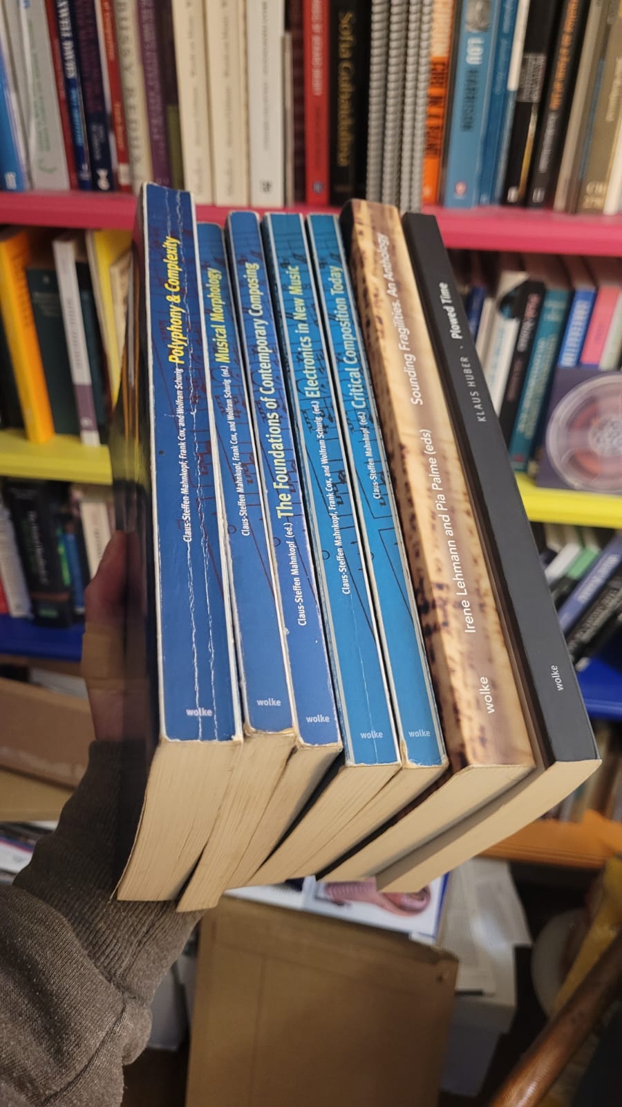 In front of shelves of music books, my outstretched hand holds several books published by Wolke Verlag
