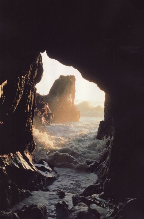 This may contain: the sun shines through an opening in a rock formation on the ocean's coast
