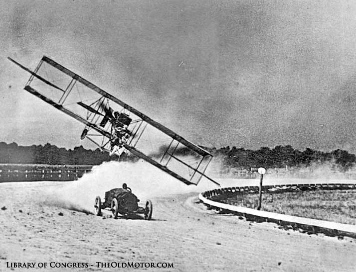 An airplane flies extremely low in a race with an automobile around a race track. An airplane flies extremely low in a race with an automobile around a race track.