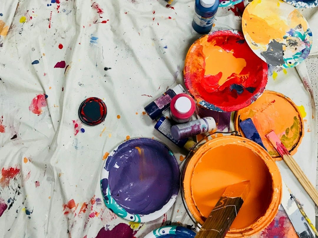 assorted-color paints and paintbrushes on white tarp