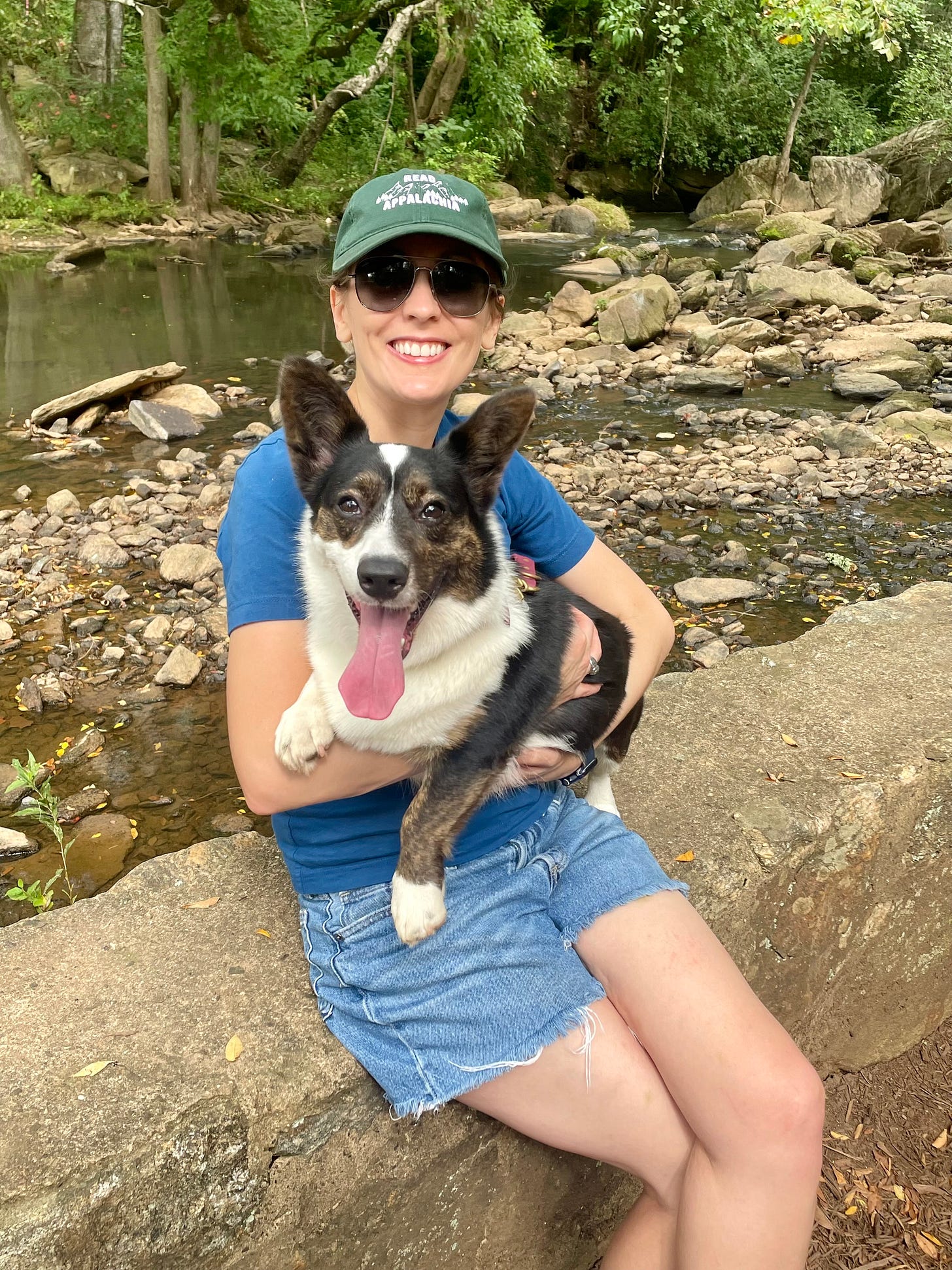 a photo of Kendra sitting on a stone wall while holding Gwen. They are both smiling at the camera.
