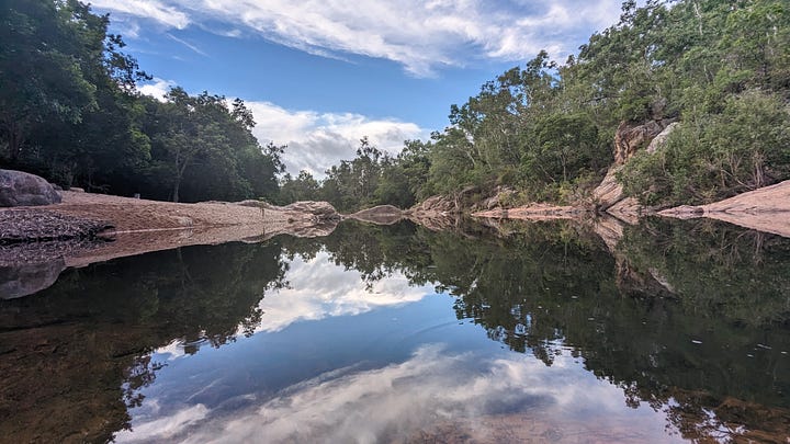 Two copies of the same image, of a small river surrounded by trees on a clear day. One of them has had the brightness adjusted by a single point, but the two images are indistinguishable.