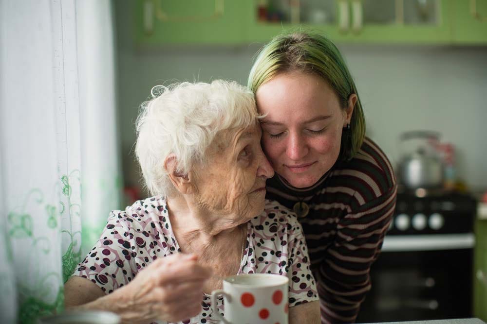 Portrait of elderly woman with her adult granddaughter at the table in the kitchen at home.