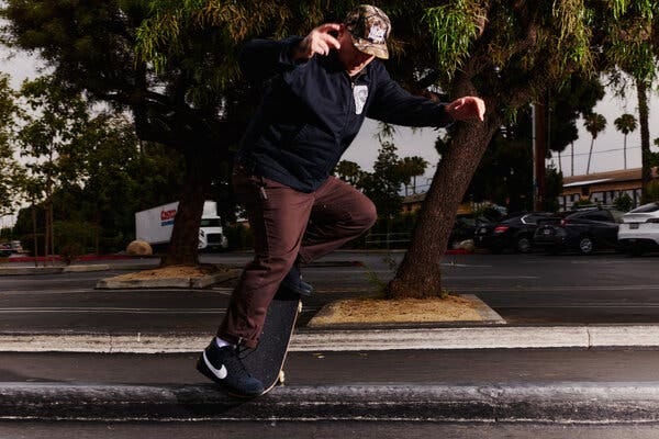 Ira Ingram on his skateboard in a parking lot, trees and cars in the background.