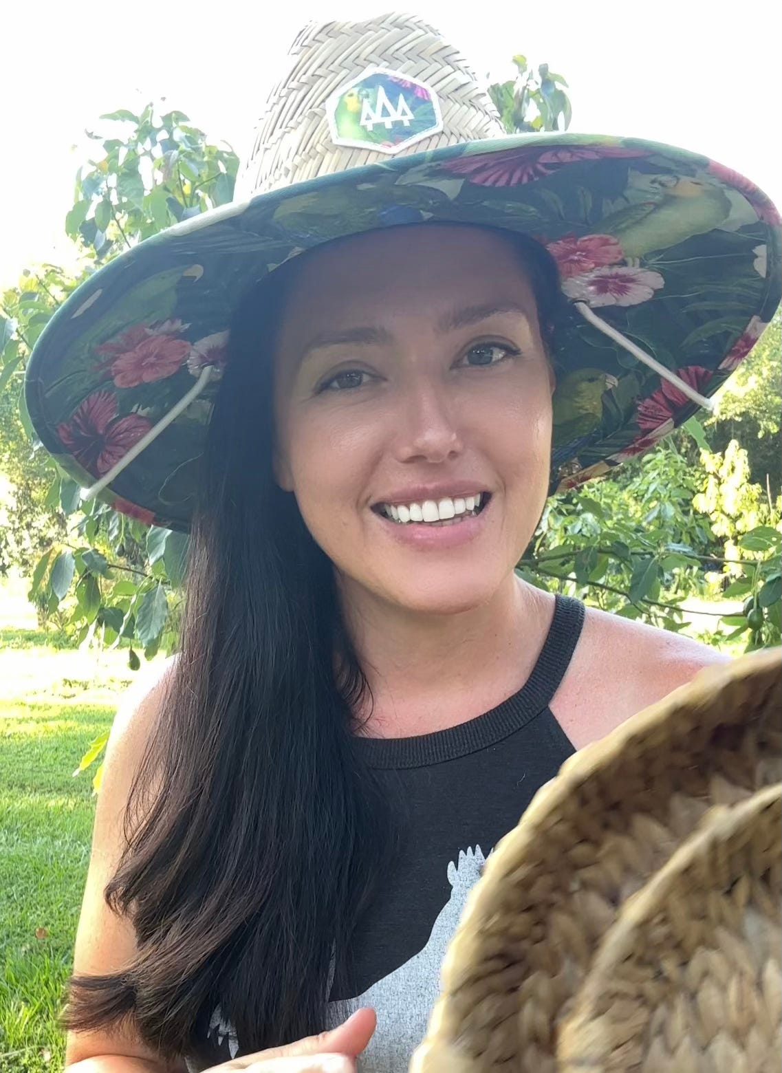Woman with long brown hair wears a multicolored wide-brimmed farming hat.
