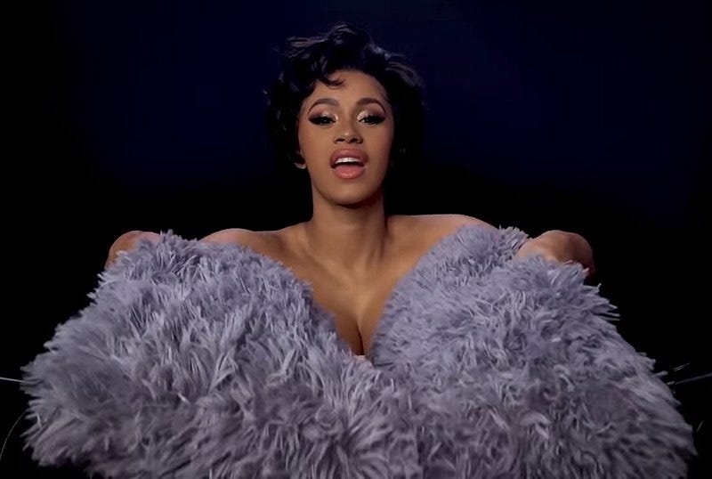 Cardi B holds fluffy grey rugs in front of her, covering stereo mics, in a goofy ASMR video Cardi B holds fluffy grey rugs in front of her, covering stereo mics, in a goofy ASMR video