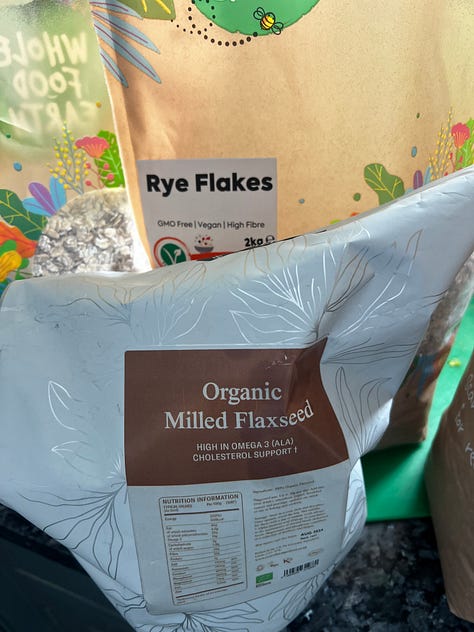 A selection of whole grain packages including rye, wheat, barley, buckwheat and flaxseed on a black stone worktop.