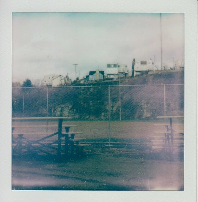 Polaroid of Fineview Field. Two rows of bleachers have a great view of the cliff face leading to Catoma Street.