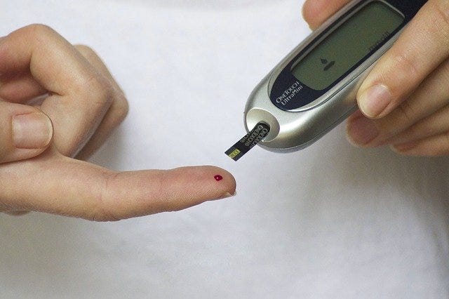 A blood glucose test strip attached to a device is held near a droplet of blood on a fingertip. A blood glucose test strip attached to a device is held near a droplet of blood on a fingertip.