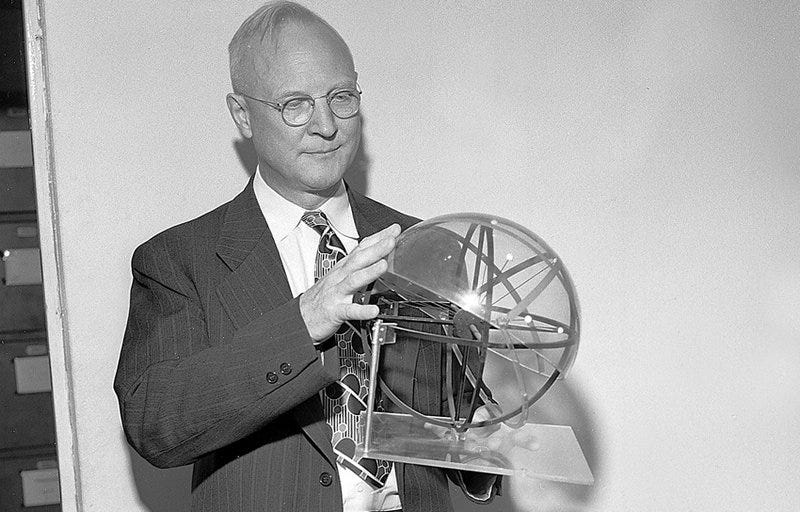 A white balding man with glasses and a suit and tie holding a transparent dome-like device