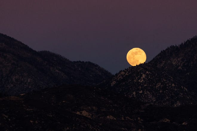 A full moon, orange from the smoke of the Eaton Fire, rises above the mountains of the Angeles National Forest north of Altadena, California, on Jan. 13, 2025.