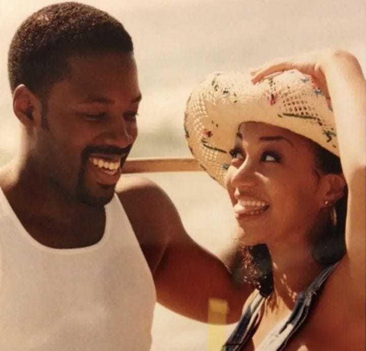 This may contain: a man and woman standing next to each other on the beach, one wearing a straw hat