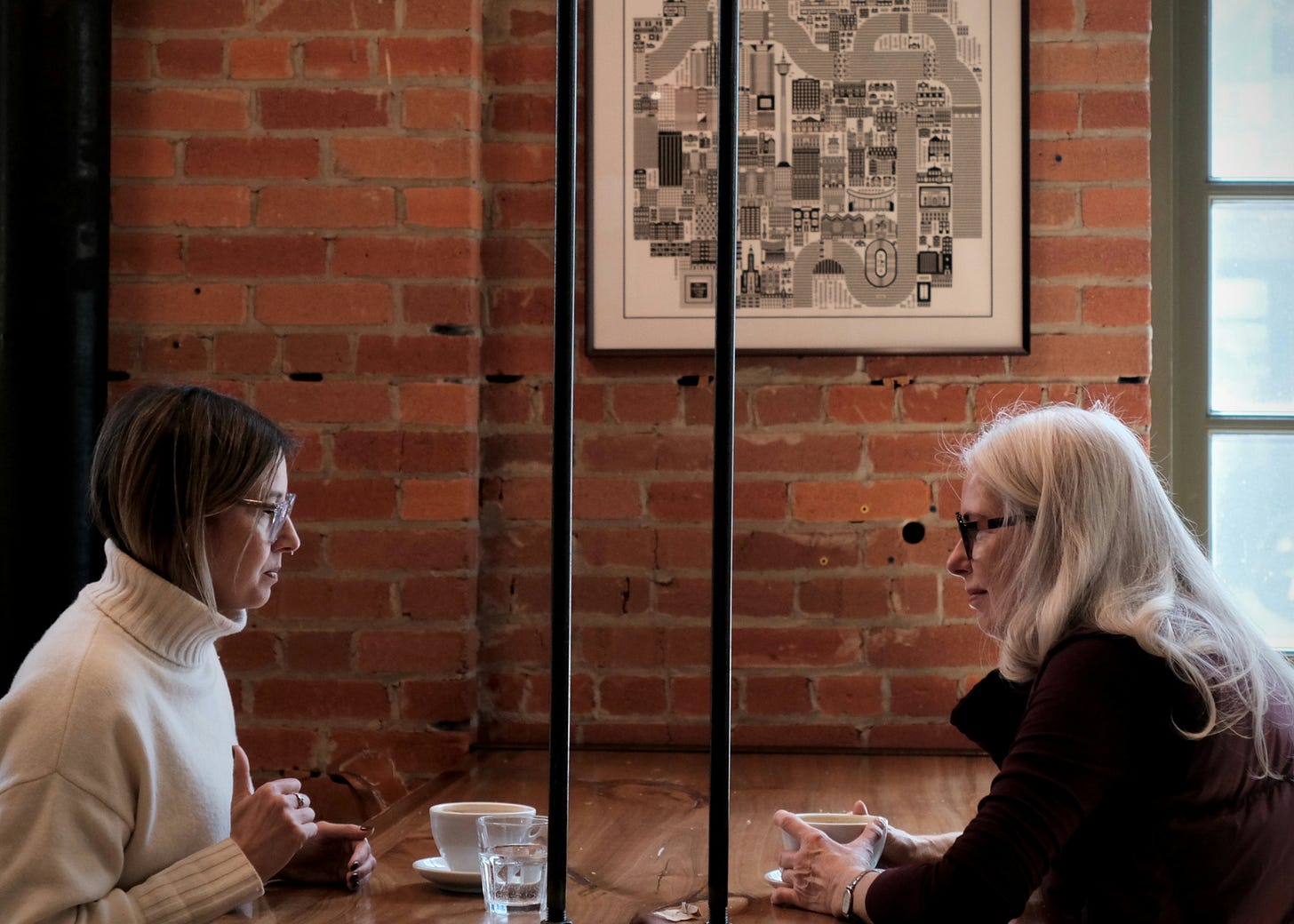 Two women sit face to face at a table. Their expressions are serious and they are making eye contact, across the table.