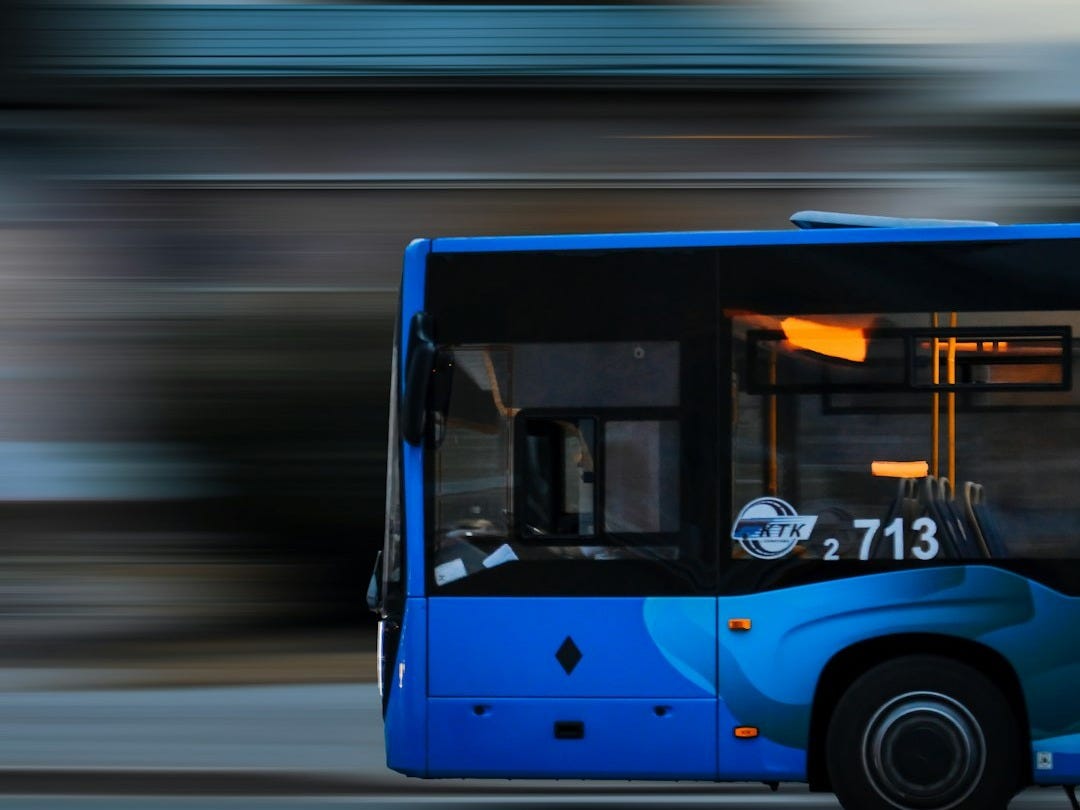a blue bus driving down a street next to a tall building a blue bus driving down a street next to a tall building