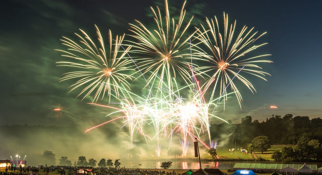 A night sky with green and orange fireworks in the sky and crowds of people below it