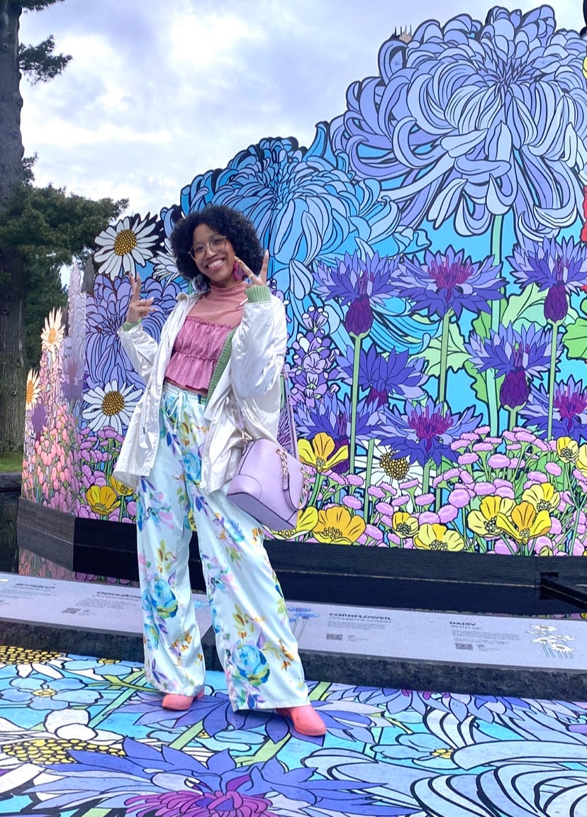 Kiana wearing colorful floral clothing standing in front of a large sculpture of Vangogh's crysanthemums brought to life
