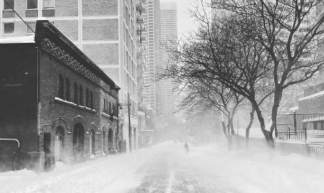 Black and white photo of a city street in a snow storm. 