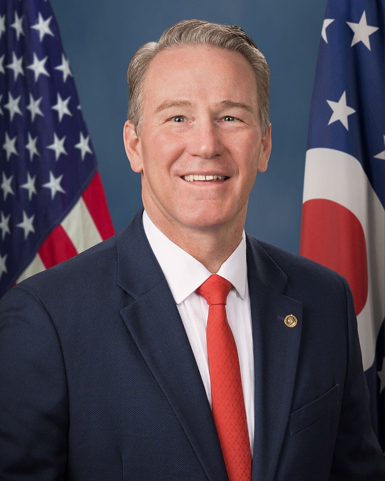 official portrait of Jon Husted; middle aged white guy with greying hair, red tie; flag in background behind him. official portrait of Jon Husted; middle aged white guy with greying hair, red tie; flag in background behind him.