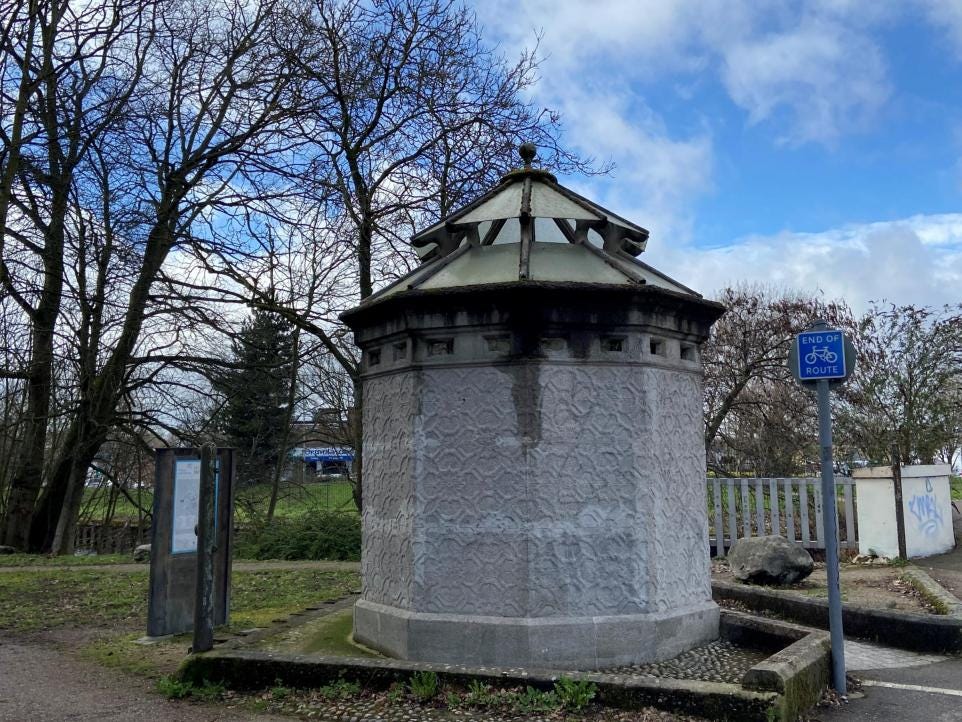 A 10-sided concrete toilet with a conical glass roof in a park in Norwich
