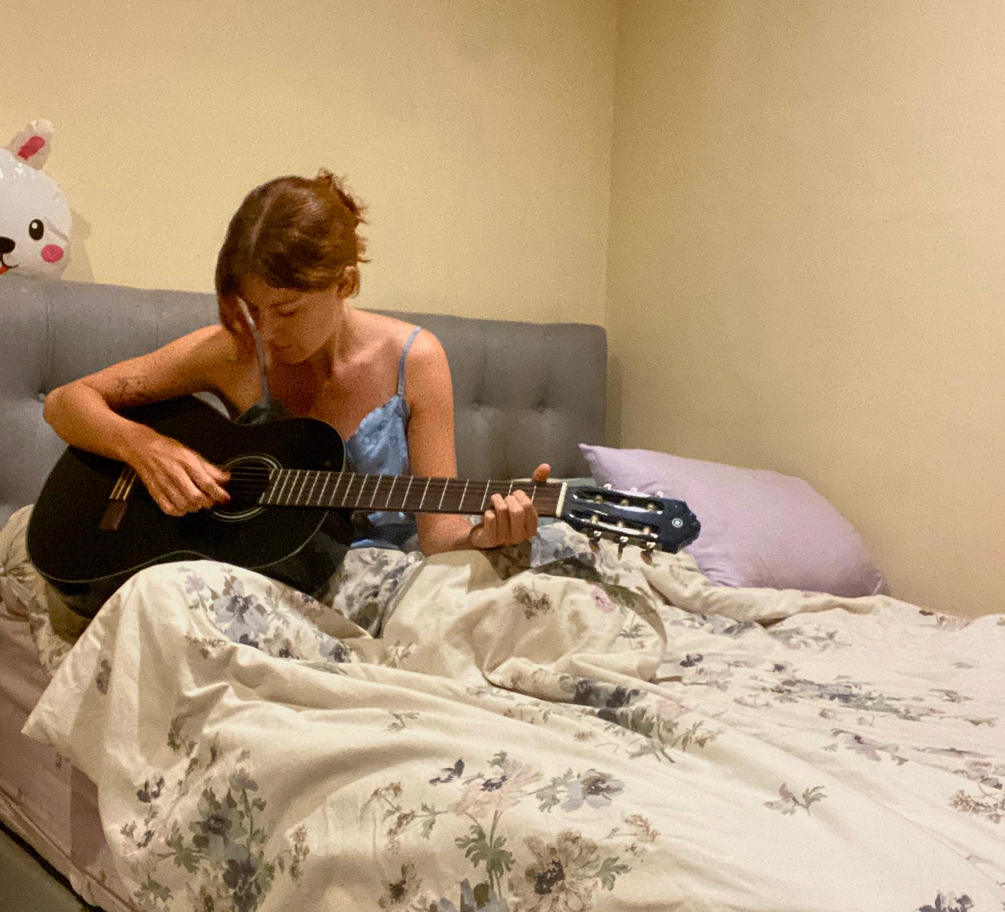Independent songwriter writing songs about family relationships plays acoustic guitar while songwriting in bed - creative process and home recording setup captured in intimate moment