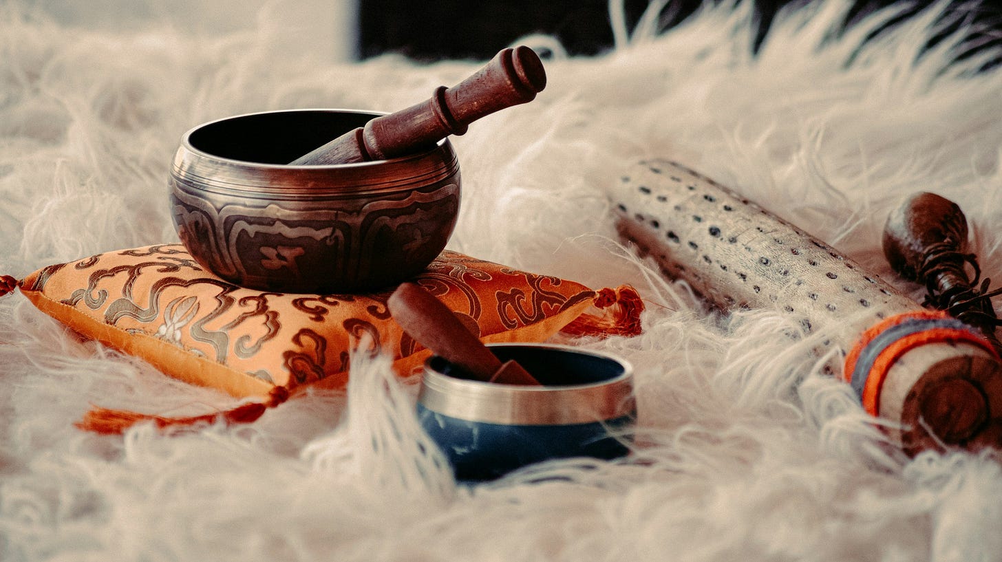 two singing bowls on what looks like a fur rug. the larger singing bowl is on an orange pillow with an intricate design.