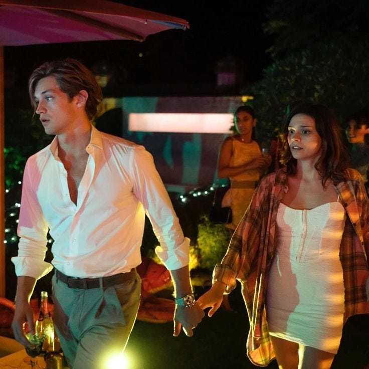 This may contain: a man and woman holding hands while walking through the night with people in the background