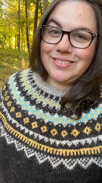Amy models her Sokatla sweater, shown in dark gray-brown, cream, yellow, and light blue.