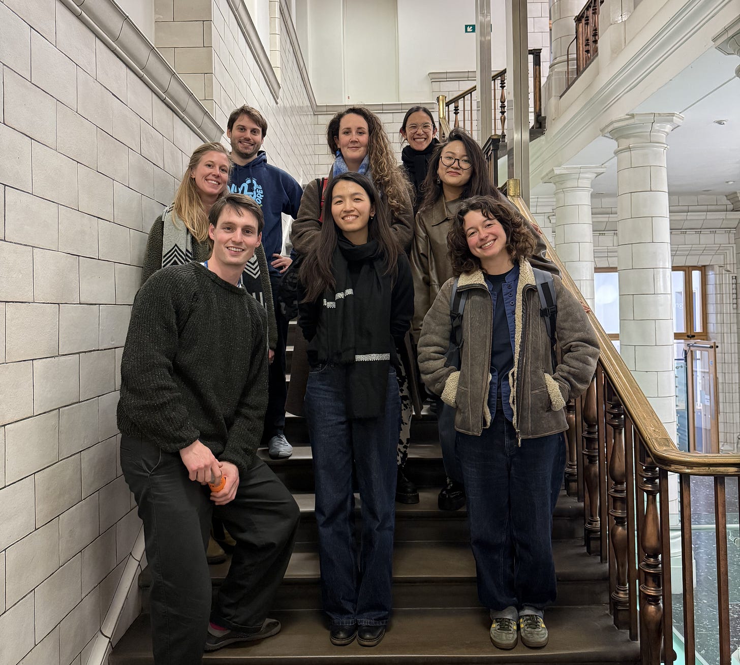A group of 8 individuals smiling on the stairs of a building. 