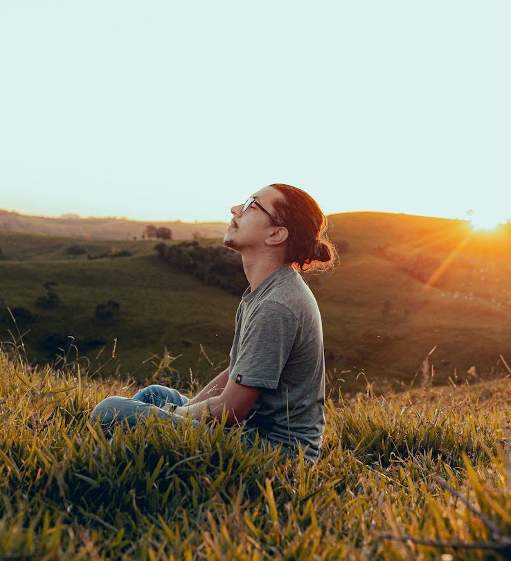 man in white shirt sitting on green grass field during sunset