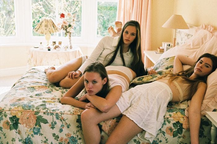This may contain: three women are laying on a bed in the same room and one is holding her leg up This may contain: three women are laying on a bed in the same room and one is holding her leg up