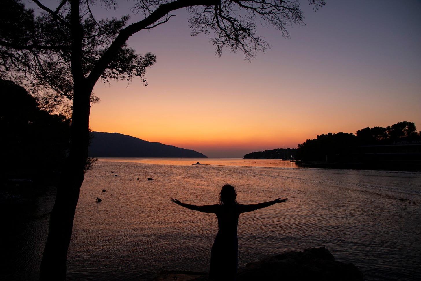 Sunset over the sea, with a black silhouette holding her arms out before it