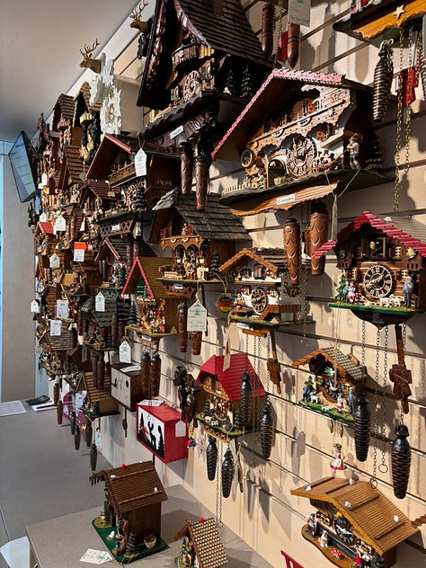a gothic cathedral, man holding a mug of beer, a plate of sausages and bread, building by a river, a wall of cuckoo clocks, closeup of a christmas musical piece in the cuckoo shop