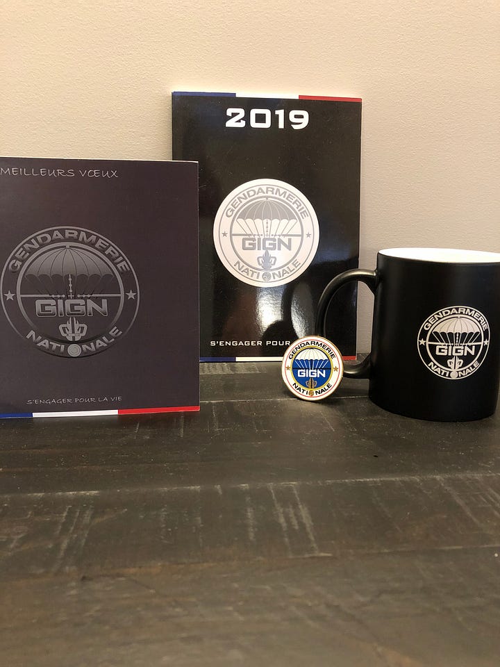 Mementos from the GIGN including a bottle of their branded champagne and two full champagne glasses.