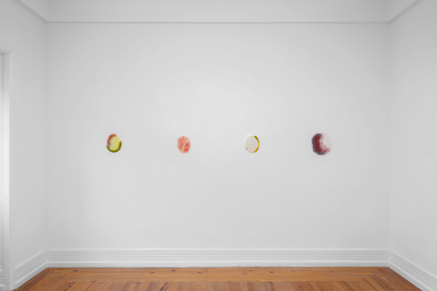 image of a gallery wall with 4 oval-shaped polychrome glass artworks