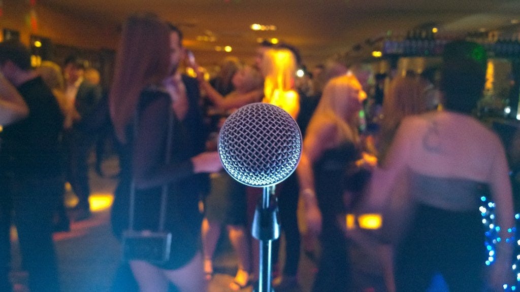 A room full of people at a New Year's Eve party, viewed from behind a microphone on the stage.