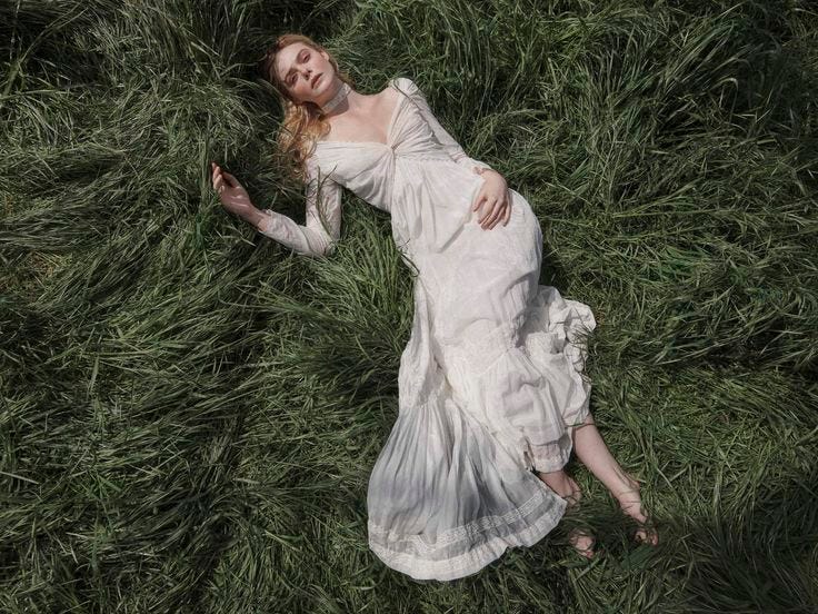 This may contain: a woman is laying in the grass with her arms out and eyes closed, wearing a white dress