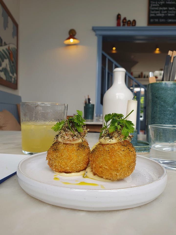 Picture one shows two crab balls topped with herbs and a glass tumbler with a drink inside. Picture two shows a tray with a dish of pickles, a dish of rice wish seaweed, a plate with a large barbecued prawn, a plate with vegetables and a cup of miso soup