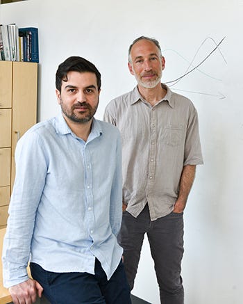 Ali Akbari and David Reich look solemnly into the camera in front of a whiteboard in Reich's office at HMS. There is an unlabeled line graph on the whiteboard. Ali Akbari and David Reich look solemnly into the camera in front of a whiteboard in Reich's office at HMS. There is an unlabeled line graph on the whiteboard.