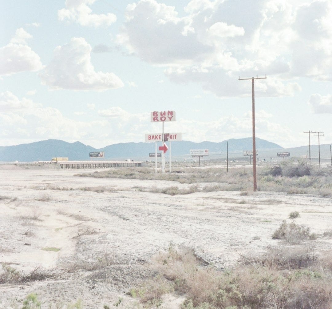 red and white road sign on brown field under white clouds and blue sky during daytime