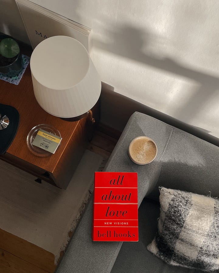 Image 1: The book All About Love and a coffee mug sit on the sofa armrest, with a glimpse of cosy decor in the background. / Image 2: A close-up of the book’s spine and coffee, with soft light and shadows playing on the wall.