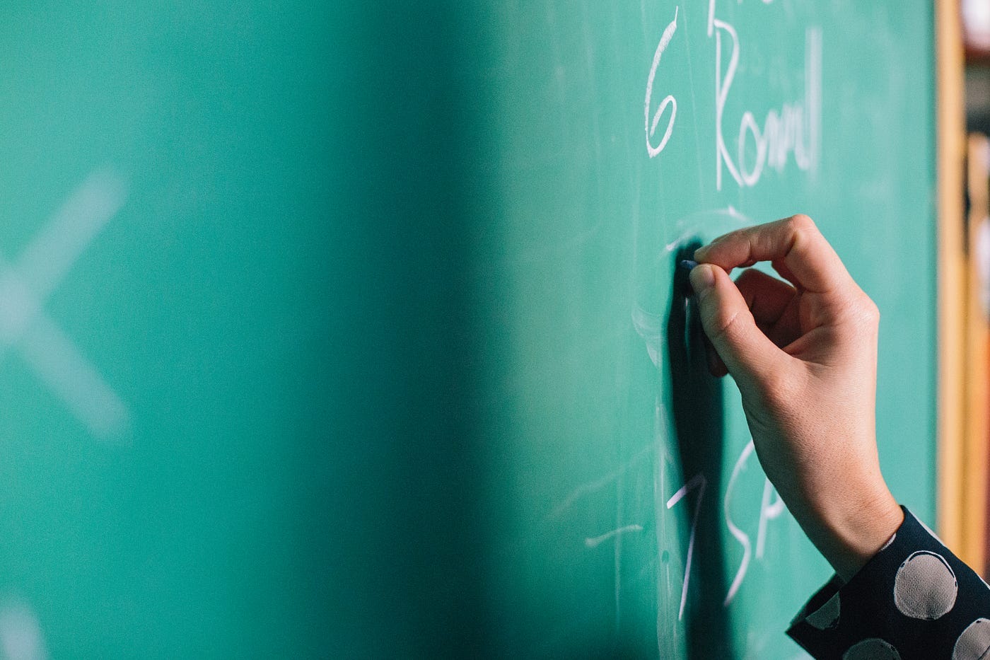 A hand holding chalk and writing on a green chalkboard